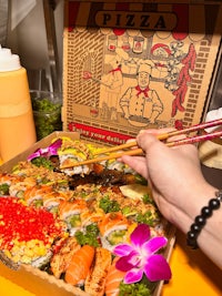 a person is holding chopsticks while eating sushi in a box